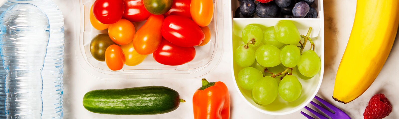 Fruits like grapes and vegetables like tomatoes in plastic containers next to a bottle of water