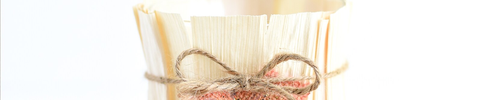 Close up of a DIY cornhusk vase wrapped with a twine ribbon tied into a bow