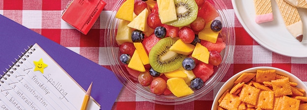 Picnic spread with fresh fruit, homework, juice boxes, cheese crackers and vanilla wafer cookies shaped like pencils